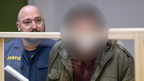Der Angeklagte wird zum Prozessauftakt von einem Justizbeamten an seinem Platz im Gerichtssaal gebracht. Der Mann soll sich in Weilheim als Polizist ausgegeben und Kinder missbraucht haben.