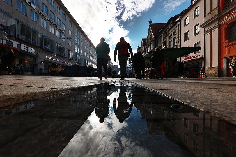 Passanten spiegeln sich in dieser Pfütze in der Neuhauser Straße.