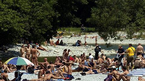 Zahlreiche Menschen liegen bei strahlendem Sonnenschein entlang der Isar in München. (Archivbild)