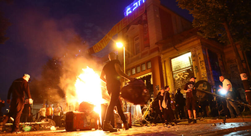 Aktivisten stehenvor der Roten Flora um eine brennende Barrikade. Knapp sechs Monate nach den schweren Ausschreitungen beim G20-Gipfel beginnen die Ermittlungen gegen einen Münchner Polizisten, der offenbar bei den Krawallen mitgewirkt haben soll.