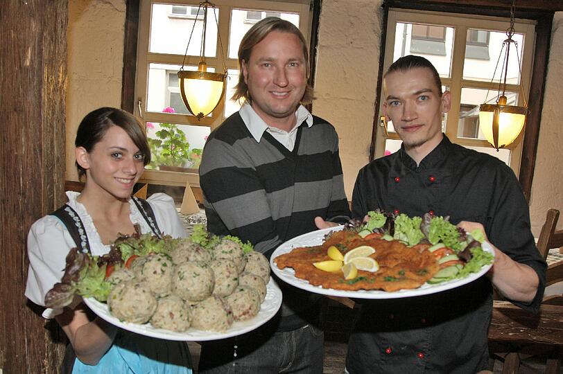 Azubine Martha, Schnitzelria-Inhaber Robert Horka und Küchenchef Erik Menzer (v. li.) mit Speckknödeln und dem Schnitzel-Riesen.