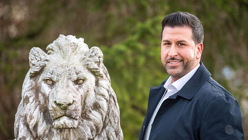 Ozan Iyibas, Bürgermeisterkandidat der CSU in Neufahrn, steht an einer Statue des Bayerischen Löwens.