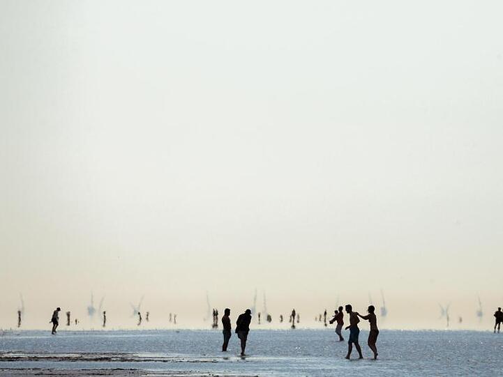 Nordseeurlauber stehen im vergangenen Sommer Wetter am Strand von Cuxhaven mit den Füßen im Wasser der auflaufenden Nordsee.