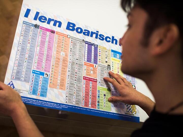 Ein Mann liest die Sprachtafel "I lern Boarisch". Foto: Alexander Heinl/dpa/Archivbild