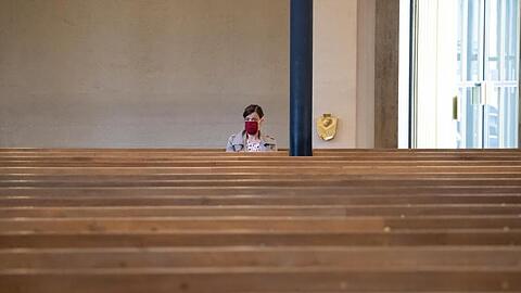 Eine Frau mit Mundschutz verfolgt einen Gottesdienst in einer Kirche. Foto: Sven Hoppe/dpa/Archivbild