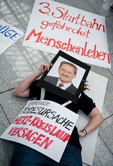 Demonstranten sitzen am Samstag (24.03.2012) am Terminal 2 des Münchner Flughafens auf Picknickdecken. Der Bund Naturschutz und das Aktionsbündnis AufgeMUCkt haben zum Protest-Picknick aufgerufen, um gegen den Bau einer dritten Startbahn am Münchner Flughafen zu demonstrieren.