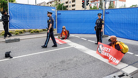 Polizisten stellen einen Sichtschutz rund um Aktivisten der Gruppierung «Letzte Generation» auf. Die Aktivisten haben sich zuvor mit den Händen auf eine Ausfahrt vom Mittleren Ring geklebt.