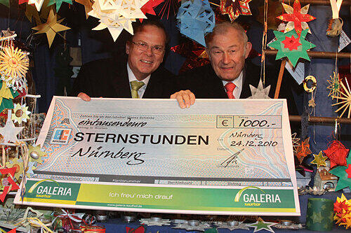 Kaufhof-Chef Walter Enders (links) überreicht Günther Beckstein am Sternstunden-Stand einen 1000-Euro-Scheck. Insgesamt kamen bei der Aktion 56.000 Euro zusammen.