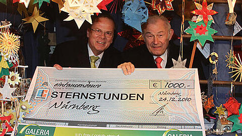Kaufhof-Chef Walter Enders (links) überreicht Günther Beckstein am Sternstunden-Stand einen 1000-Euro-Scheck. Insgesamt kamen bei der Aktion 56.000 Euro zusammen.