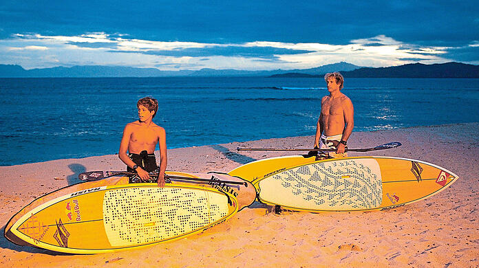 Super-Surfer Robby Naish am Strand mit einem jungen Kollegen am Strand. Foto: ZDF und www.redbullmediahouse.com/Tom Servais