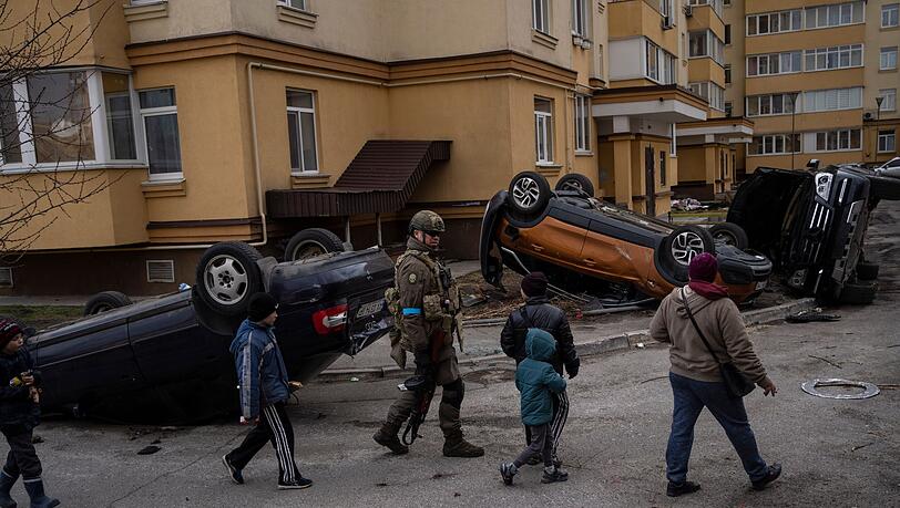 Ein ukrainischer Soldat geht in Butscha mit Kindern an zerstörten Autos vorbei.