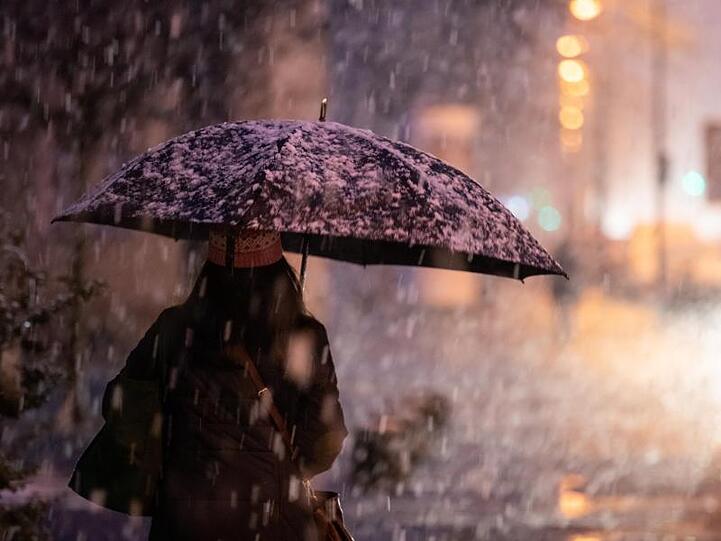 Eine Frau geht bei Schneefall auf dem Gehsteig. Foto: Daniel Karmann/dpa