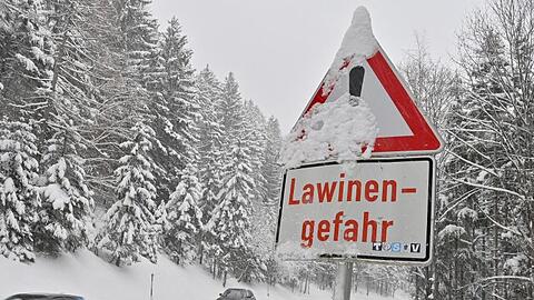 PKW fahren an einem "Lawinengefahr"-Schild vorbei.