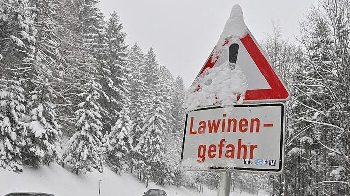 PKW fahren an einem "Lawinengefahr"-Schild vorbei.