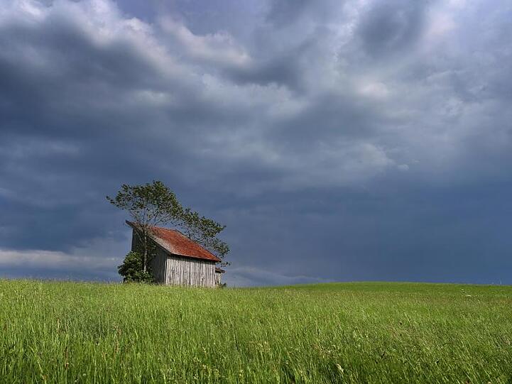 Dunkle Regenwolken ziehen über eine Holzhütte auf. Foto: Karl-Josef Hildenbrand/dpa/Archivbild