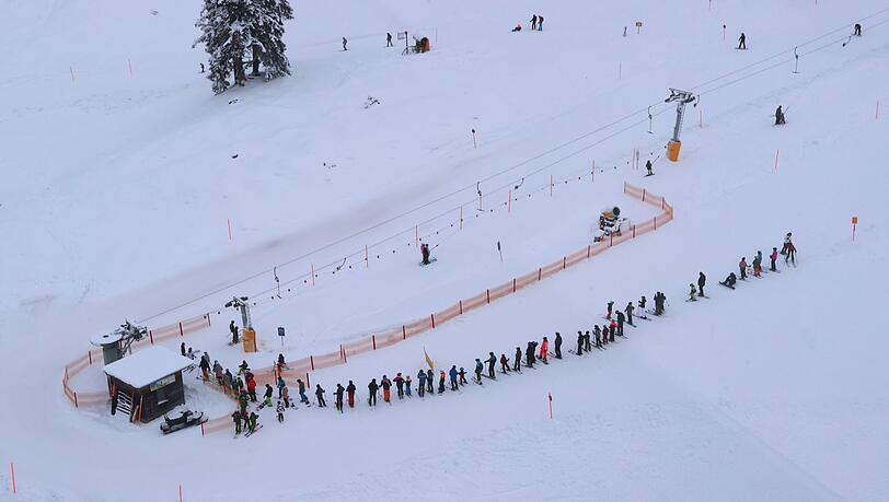 Kinder und Erwachsene stehen an einem Kinderschlepplift am Nebelhorn in einer Reihe.