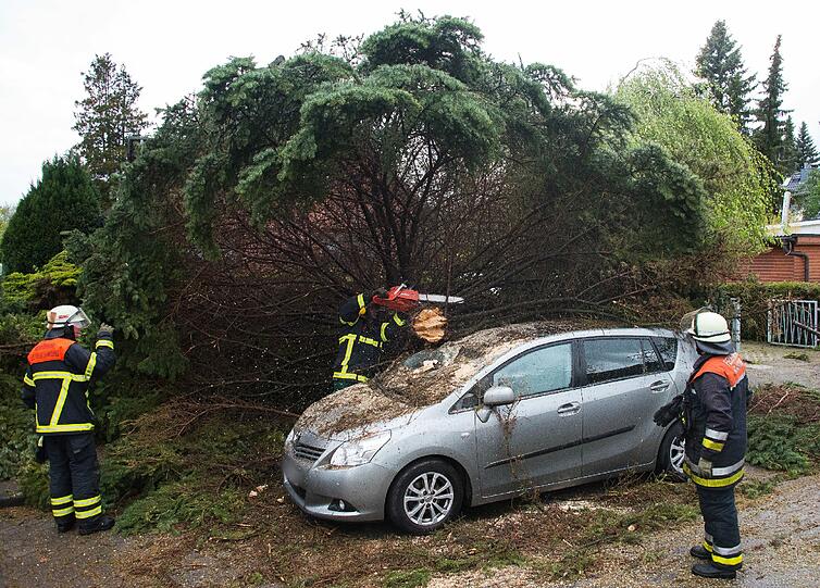 Ein Feuerwehrmann zersägt in Hamburg-Rahlstedt einen auf ein Auto gestürzten Baum.