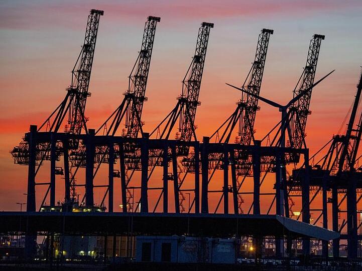 Die Sonne geht hinter den hochgeklappten Containerbrückenkränen, die normalerweise Schiffe entladen, im Hamburger Hafen unter.