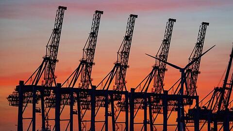 Die Sonne geht hinter den hochgeklappten Containerbrückenkränen, die normalerweise Schiffe entladen, im Hamburger Hafen unter.