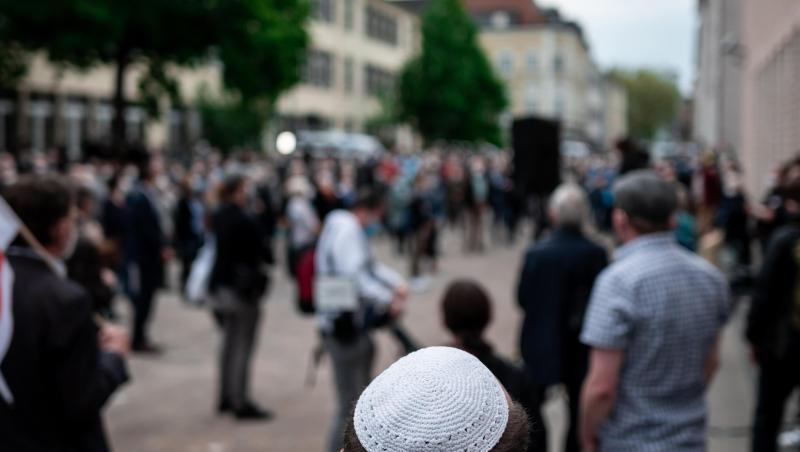 Menschen stehen bei einer Solidaritätskundgebung in Gelsenkirchen auf dem Platz vor der Synagoge. Dabei trägt ein Mann eine Kippa.