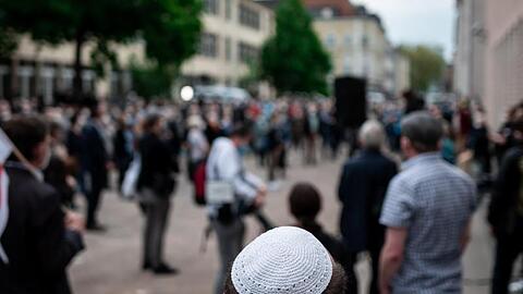 Menschen stehen bei einer Solidaritätskundgebung in Gelsenkirchen auf dem Platz vor der Synagoge. Dabei trägt ein Mann eine Kippa.