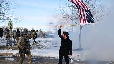 Ein Protestierender mit einer amerikanischen Flagge steht einem ICE-Beamten gegen&uuml;ber.