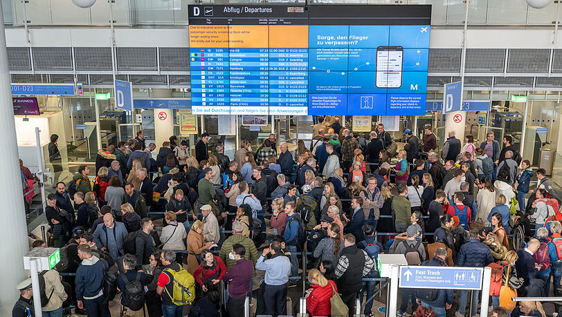 Zu Pfingsten wird's am Flughafen München wieder voll: Passagiere stehen in der Abflughalle in Schlangen an, um zur Sicherheitskontrolle zu gelangen. (Archivbild)