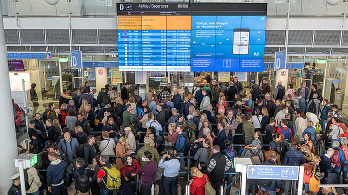 Zu Pfingsten wird's am Flughafen München wieder voll: Passagiere stehen in der Abflughalle in Schlangen an, um zur Sicherheitskontrolle zu gelangen. (Archivbild)