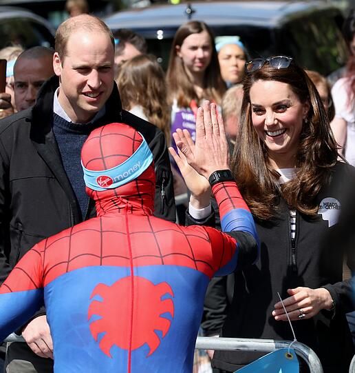 Während der britische Prinz William und seine Frau, Herzogin Kate, den Läufern Wasserflaschen reichen, begrüßt sie ein Läufer im Spider Man-Kostüm.