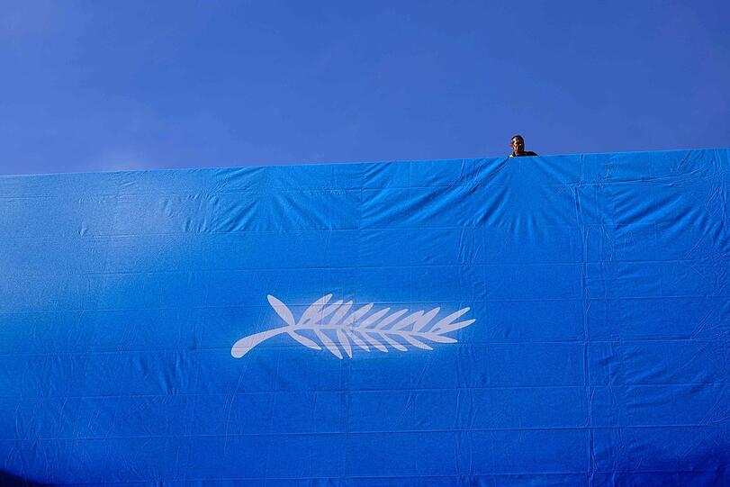 Ein Arbeiter hängt das offizielle Plakat der 77. Filmfestspiele von Cannes an der Fassade des Palais des Festivals auf.
