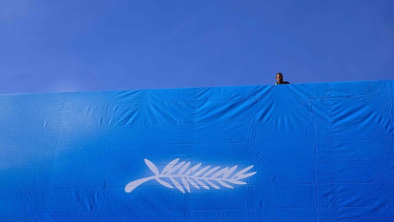 Ein Arbeiter hängt das offizielle Plakat der 77. Filmfestspiele von Cannes an der Fassade des Palais des Festivals auf. Ein Arbeiter hängt das offizielle Plakat der 77. Filmfestspiele von Cannes an der Fassade des Palais des Festivals auf.