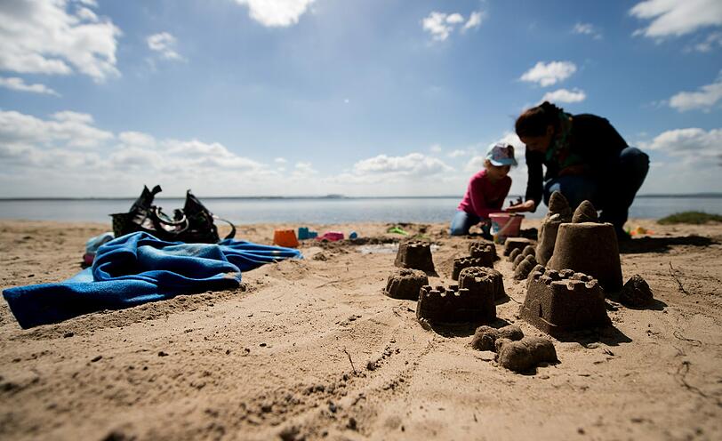 Eine Frau baut am Steinhuder Meer bei Mardorf mit ihrem Kind Sandburgen am Strand.