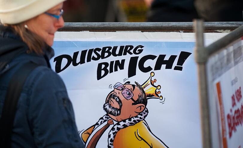 Passanten betrachten am Donnerstag in Duisburg eine Karikatur des Kuenstlers Martin Tazl vom Oberbuergermeister von Duisburg, Adolf Sauerland (CDU), mit der Ueberschrift "Duisburg bin ich!" und der Unterschrift "Nicht mehr lange!!!"