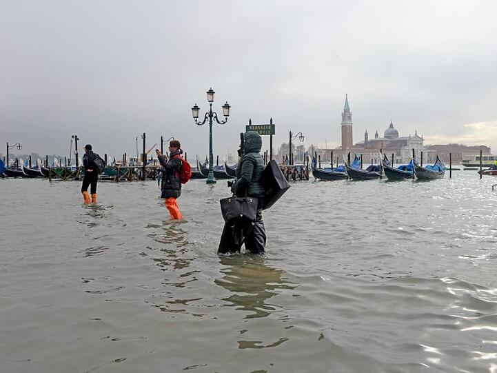 Immer auf den Wegen bleiben: Menschen waten unweit des Ufers zum "Bacino San Marco" durchs überflutete Venedig.