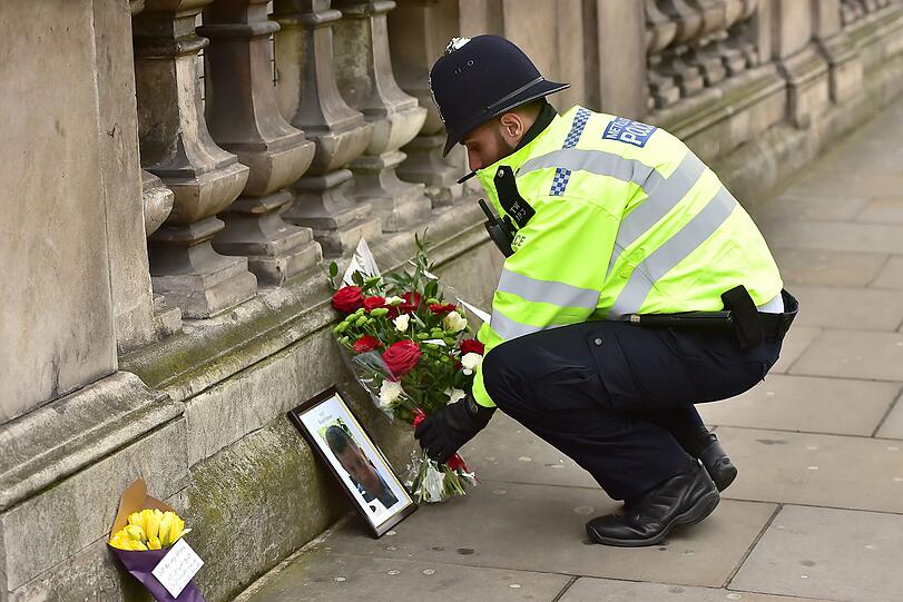 23.03.2017:  Ein Polizist legt Blumen an einem Foto in der Nähe des britischen Parlament in London nieder. Bei einem Terroranschlag auf der Westminster-Brücke und am Parlament im Herzen Londons hat ein Angreifer mindestens drei Menschen getötet und rund 40 weitere teils schwer verletzt. Der Täter wurde erschossen, nachdem er einen Polizisten niedergestochen hatte.