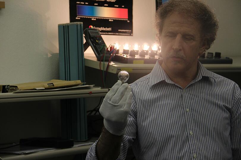 Josef Stieger zeigt eine Signalglühlampe, wie sie momentan bei der DB verwendet wird. Ihre durchschnittliche Brenndauer beträgt 6-10 Monate, präventiv werden die Lampen alle 6 Monate ausgetauscht. Auch hier liegt die LED Lampe mit einer Lebenserwartung von 10 Jahren vorn.