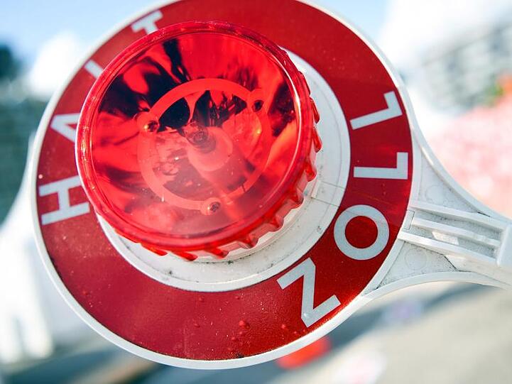 Ein Mann hält eine Winkerkelle mit der Aufschrift "Halt Zoll". Foto: picture alliance / Christophe Gateau/dpa/Archiv/Illustration