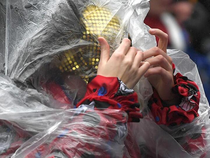 Eine Frau schützt sich mit einem Poncho vor dem Regen beim Rosenmontagszug in Köln (Archiv). Auch in diesem Jahr soll es in den Karnevalshochburgen nass werden.