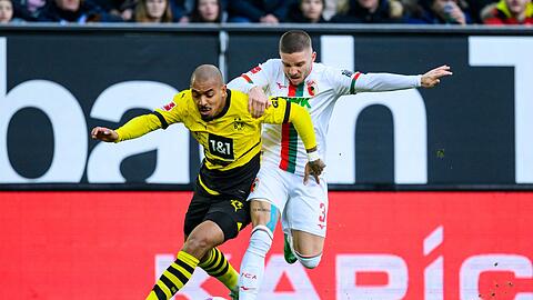 Dortmunds Donyell Malen (l) versucht den Ball vor Augsburgs Mads Pedersen (r) zu behaupten.