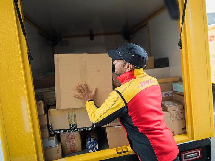 Ein Paketzusteller stellt ein Paket in ein Fahrzeug der Deutschen Post DHL.