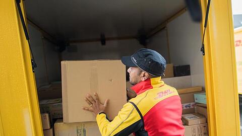 Ein Paketzusteller stellt ein Paket in ein Fahrzeug der Deutschen Post DHL.