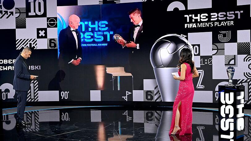 Dem FCB-Stürmer Robert Lewandowski (r. auf Bildschirm) wird 2020 die Weltfußballer-Trophäe überreicht.