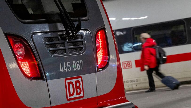 Eine Regionalbahn und ein ICE der Deutschen Bahn stehen nebeneinander im Hauptbahnhof, während eine Frau mit einem Koffer vorbeiläuft.