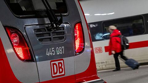 Eine Regionalbahn und ein ICE der Deutschen Bahn stehen nebeneinander im Hauptbahnhof, während eine Frau mit einem Koffer vorbeiläuft.