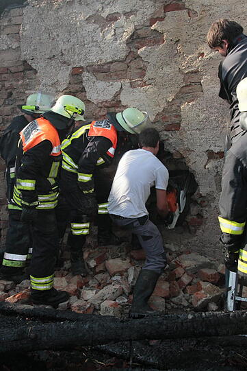 Hinter einer eingestürzten Mauer im abgebrannten Bauernhof ist noch ein Kuhkalb eingesperrt. Mit bloßer Hand und einem Geißbein durchbrechen die Feuerwehrleute eine 50 Zentimeter dicke Mauer und retten es.