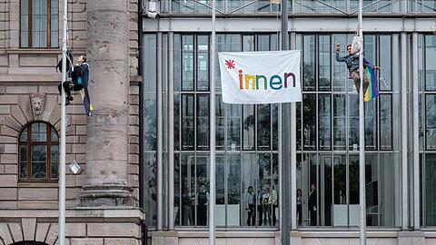 Zwei Menschen haben einen Fahnenmast vor der Bayerischen Staatskanzlei in München erklommen, um gegen das bayerische Genderverbot zu demonstrieren.