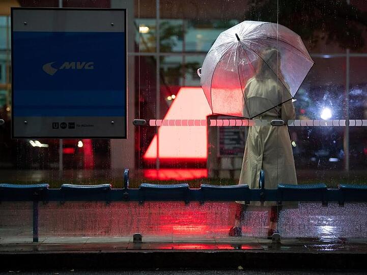 Eine Frau wartet mit ihrem Regenschirm an einer Bushaltestelle auf den Bus. Foto: Sven Hoppe