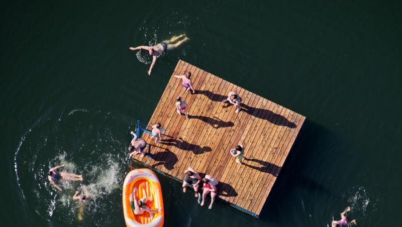 Kinder toben auf einer Holzinsel und in einem Schlauchboot in einem See (Luftaufnahme). Foto: Julian Stratenschulte/Archivbild