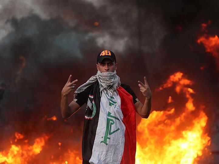 Ein Demonstrant zeigt vor lodernden Flammen das Siegeszeichen. In mehreren Provinzen stürmten die Protestler Gebäude und legten Feuer. Viele Iraker klagen über die vernachlässigte Infrastruktur sowie über die Arbeitslosigkeit.