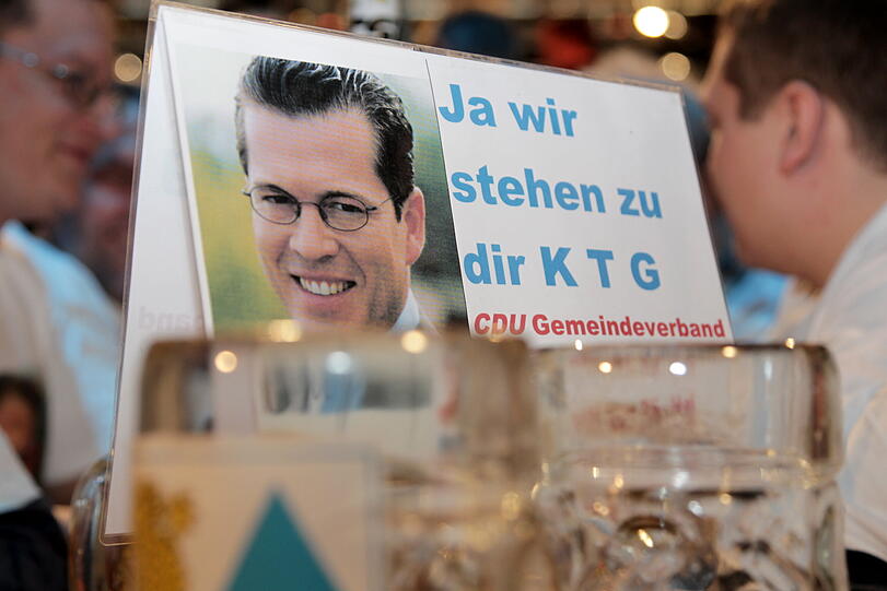 Ein Schild mit einem Foto des zurueckgetretenen Verteidigungsministers Karl-Theodor zu Guttenberg (CSU) und der Aufschrift "Ja wir stehen zu Dir K T G. CDU Gemeindeverband" steht am Mittwoch in Passau in der Dreilaenderhalle beim Politischen Aschermittwoch 2011 der CSU auf einem Biertisch.